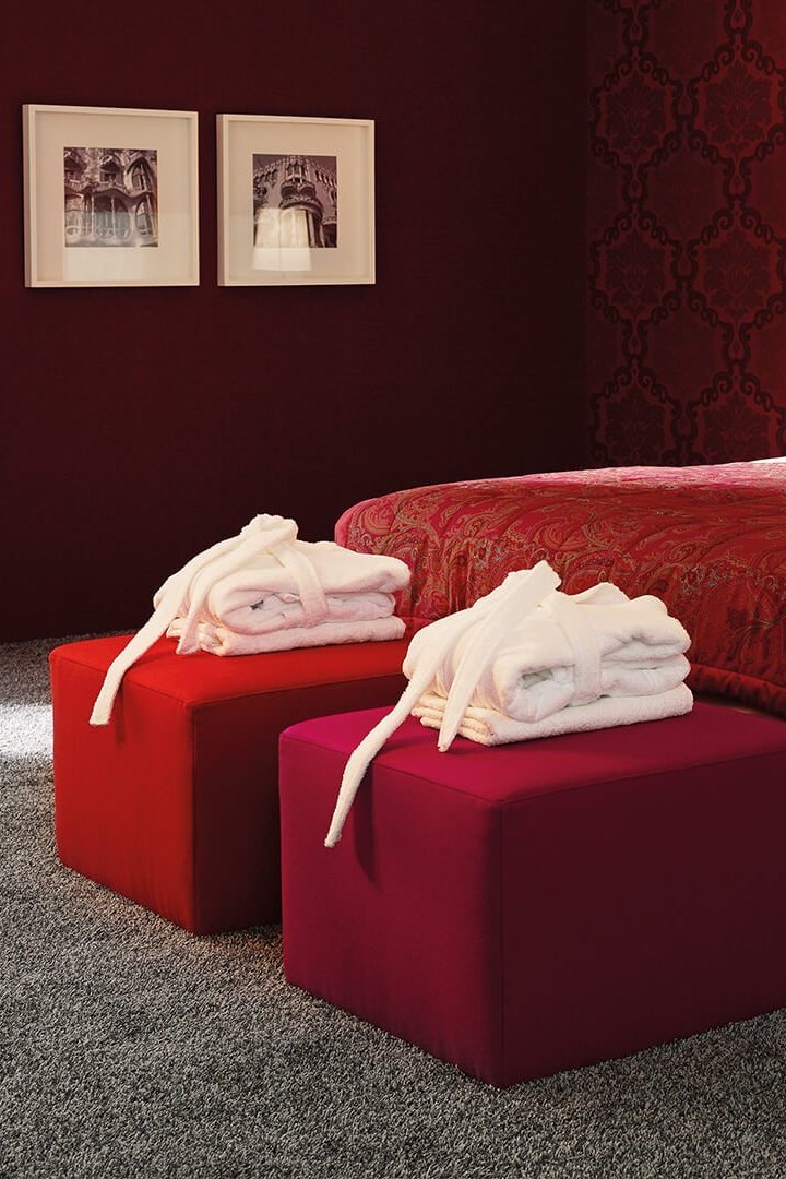 Weißes JOKA Noblesse Boxspringbett mit zwei roten Höckern und roter Wandgestaltung