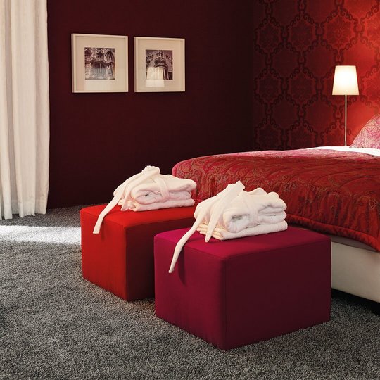 Weißes JOKA Noblesse Boxspringbett mit zwei roten Höckern und roter Wandgestaltung