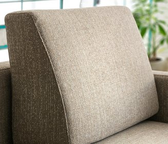 Nahaufnahme eines keilförmig nach oben zulaufenden Formkissens aus braun-beige meliertem Webstoff auf der Rückenlehne des Sofas.
