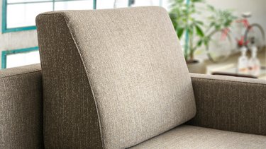 Nahaufnahme eines keilförmig nach oben zulaufenden Formkissens aus braun-beige meliertem Webstoff auf der Rückenlehne des Sofas.