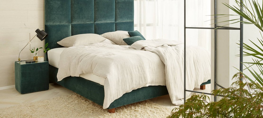Modernes JOKA Piazza Boxspringbett mit grünem Samt-Kopfteil und hellem Bettzeug in hellgrünem Schlafzimmer