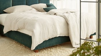 Modernes JOKA Piazza Boxspringbett mit grünem Samt-Kopfteil und hellem Bettzeug in hellgrünem Schlafzimmer