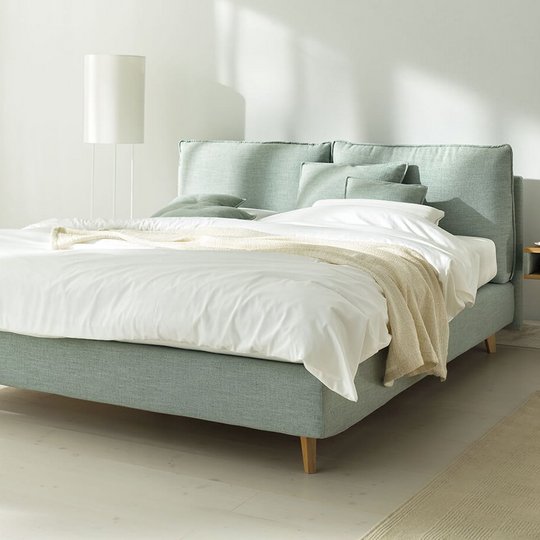 JOKA Arte Boxspringbett in Hellgrün mit weißer Bettwäsche und Holzfüßen im hellen Schlafzimmer