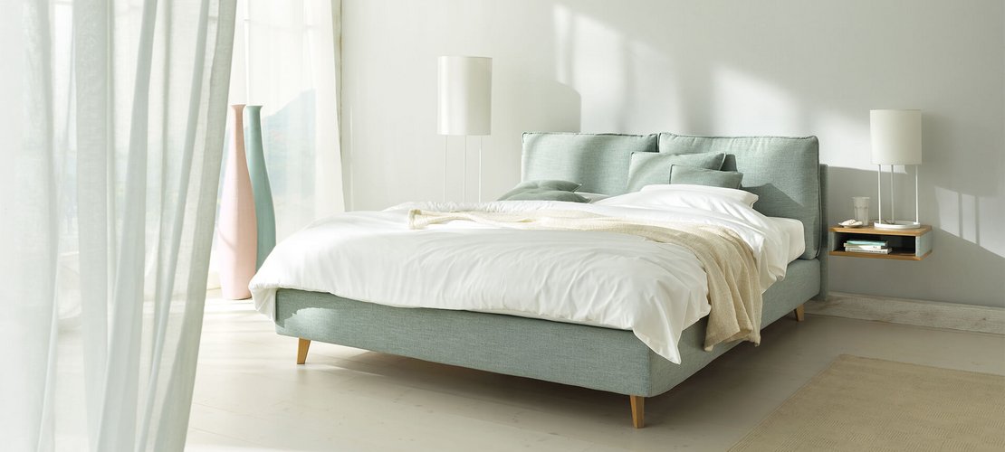JOKA Arte Boxspringbett in Hellgrün mit weißer Bettwäsche und Holzfüßen im hellen Schlafzimmer