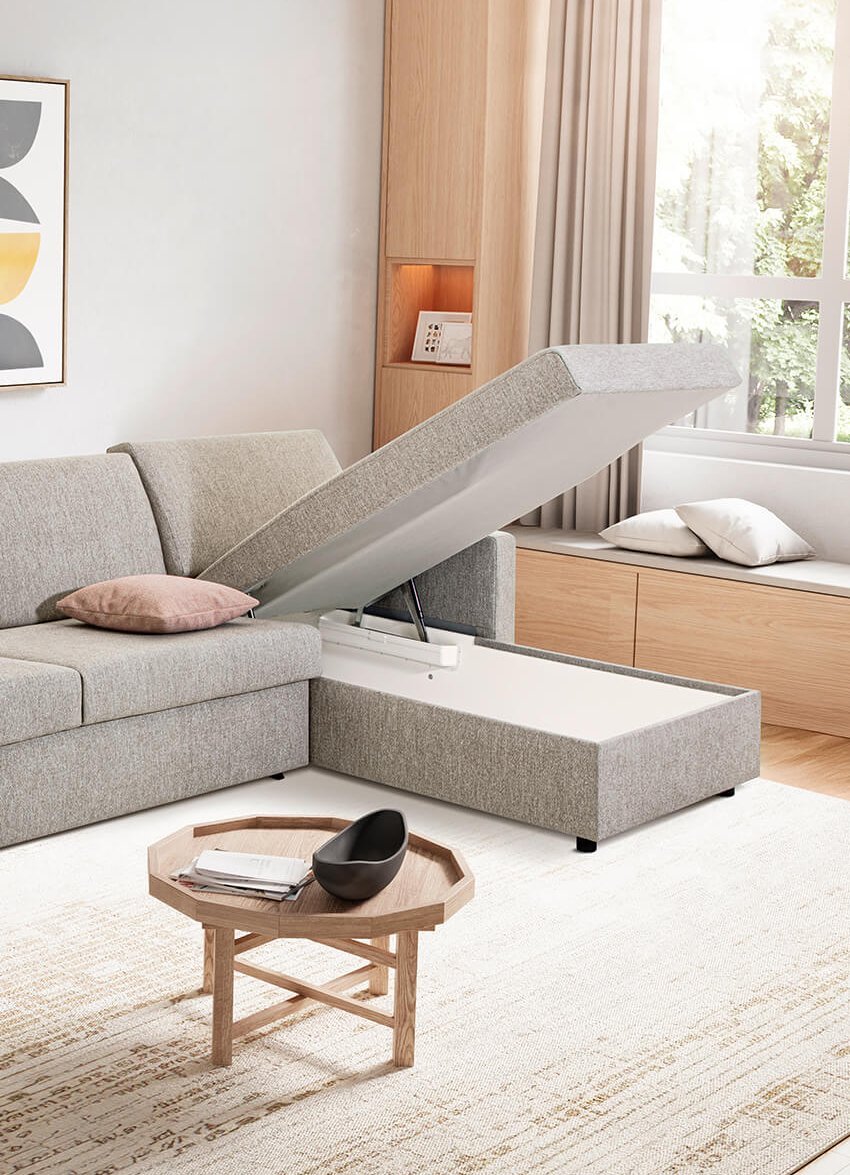 JOKA Marea L-förmiges Eckschlafsofa in Grau mit hochgeklappter Récamiere und offenem Stauraum.