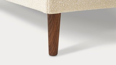 Nahaufnahme eines geraden, kegelförmigen Holzfußes unter der hellen Polsterung.