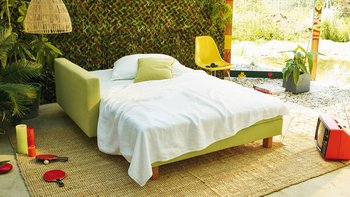 JOKA Quadro Schlafsofa in Hellgrün, ausgeklappt als Bett mit weißer Bettwäsche und Kissen.