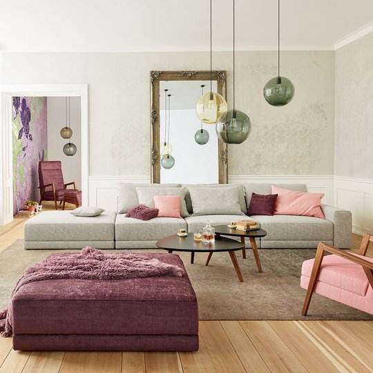 Joka Laguna großzügige graue Wohnlandschaft mit rosa Sessel, dunkelviolettem Hocker und Kamin