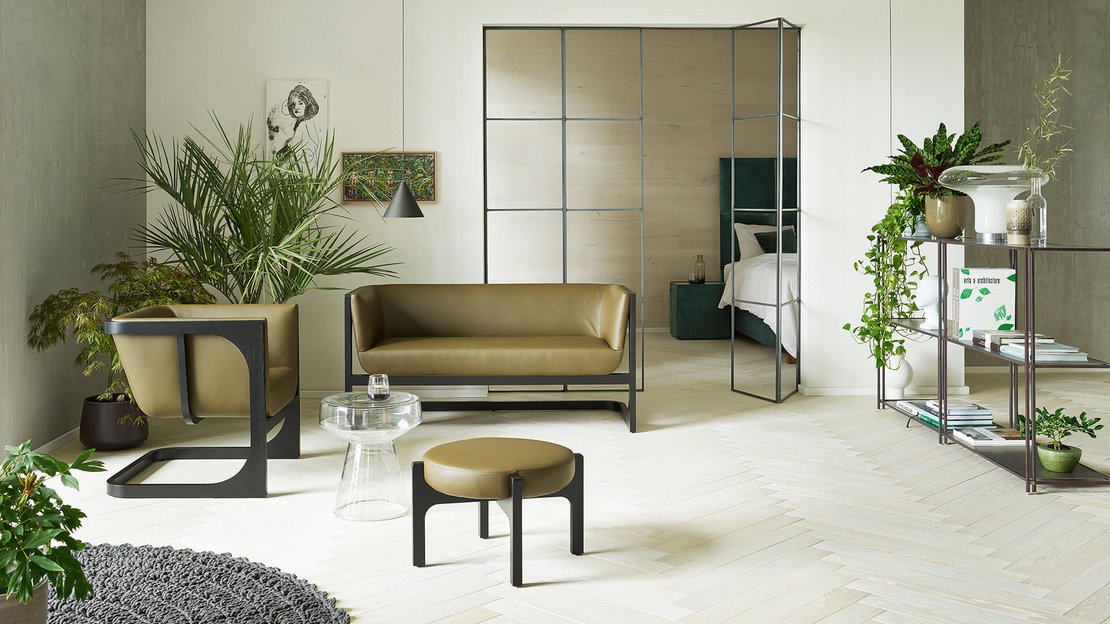Hell eingereichtes Wohnzimmer mit JOKA Corso Sessel, Sofa, Hocker, Pflanzen und Regalelement