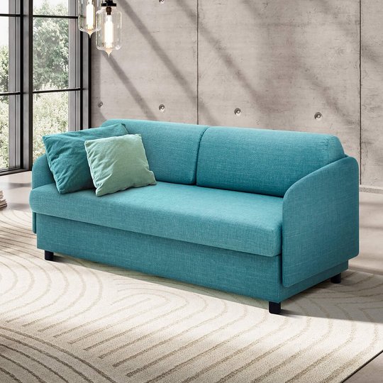 Gesamtansicht des türkisblauen JOKA Pure Allraumbetts mit zweiseitigem Umbau, Rückenkissen und Zierkissen in einem modernen Wohnzimmer