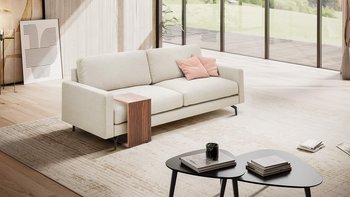 Helles, modernes Wohnzimmer mit einem hellen 3-Sitzer-Sofa, an das ein passender Holz-Beistelltisch geschoben ist.