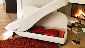 Weißes Recamiere-Sofa mit hochgeklapptem Staufach und Kissen vor einem Kamin