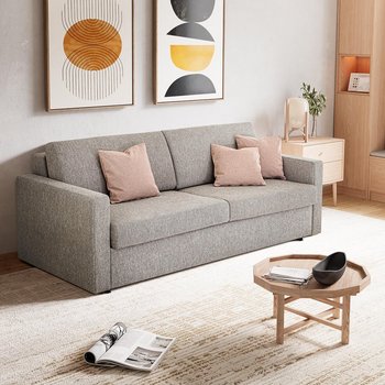 JOKA Marea Längsschläfer in Grau mit drei rosafarbenen Zierkissen in einem hellen, modern eingerichteten Wohnraum mit Teppich und großen Fenstern.