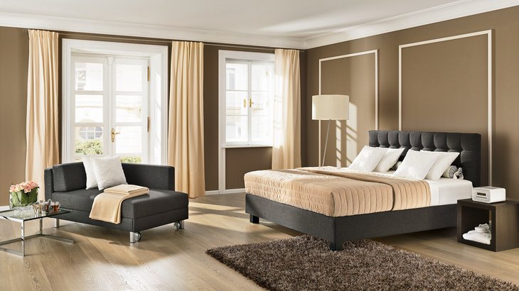 Dunkelgraues JOKA Noblesse Nouvelle Boxspringbett und passende Recamiere in warmem, braunem Raum