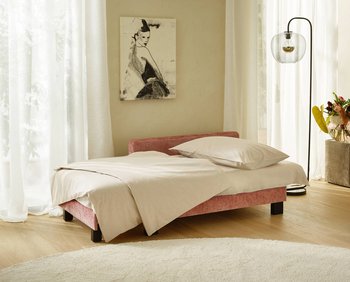 Alternative Aufnahme der altrosafarbenen JOKA Recamiere in Bett-Konfiguration mit cremefarbener Bettwäsche im lichtdurchfluteten Hotelzimmer.