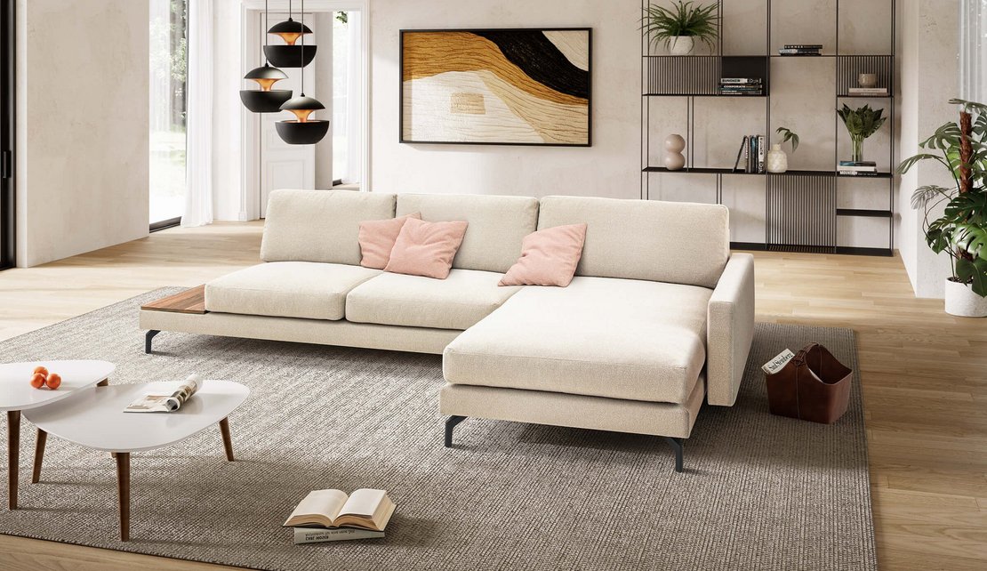 Großzügige helle Wohnlandschaft mit integrierter Holzablage und schwarzen Metallfüßen auf einem beigefarbenen Teppich.