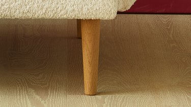 Detailaufnahme des konischen Holzfußes unter dem hellen Bouclé-Bezug des Sofas.