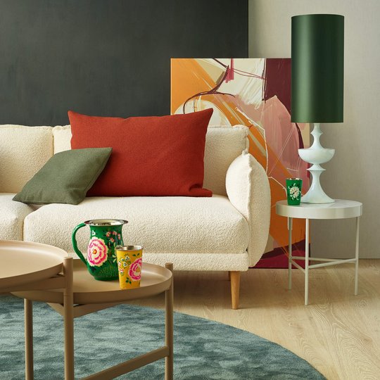 Hochformatiges Detailfoto eines weißen Bouclé-Sofas mit rotem und grünem Kissen neben einem Couchtisch.