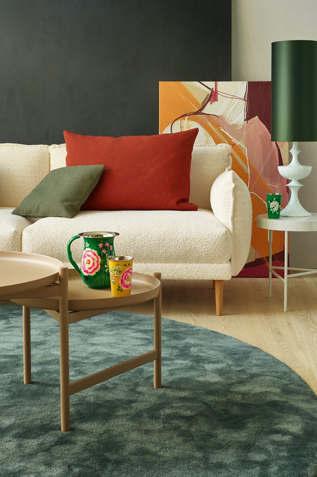 Hochformatiges Detailfoto eines weißen Bouclé-Sofas mit rotem und grünem Kissen neben einem Couchtisch.
