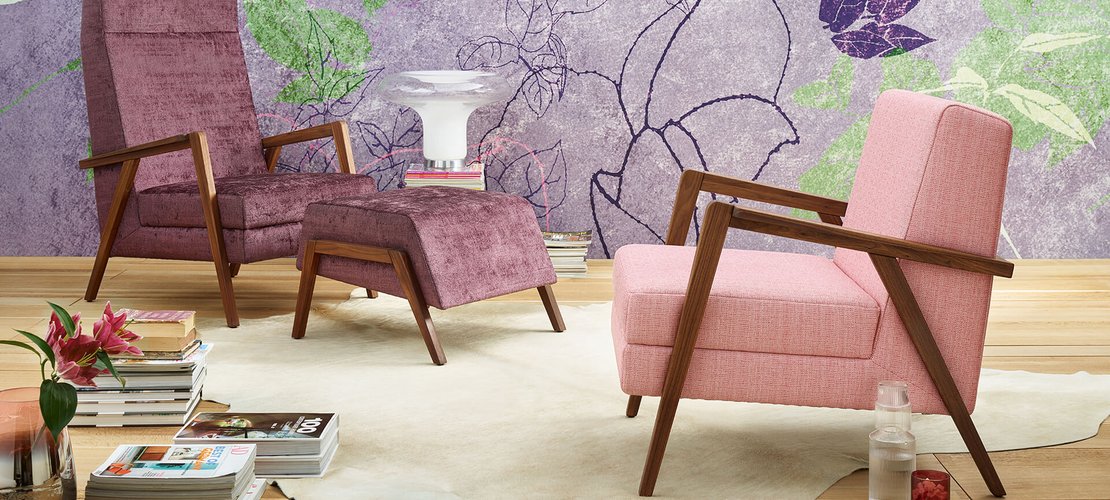 oka Laguna lilafarbener und rosa Fauteuil mit Hocker vor floral gemusterter Tapete