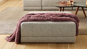 Joka Laguna helle Couchlandschaft in Grau mit dunklem Couchtisch und rosa Fauteuil im Hintergrund