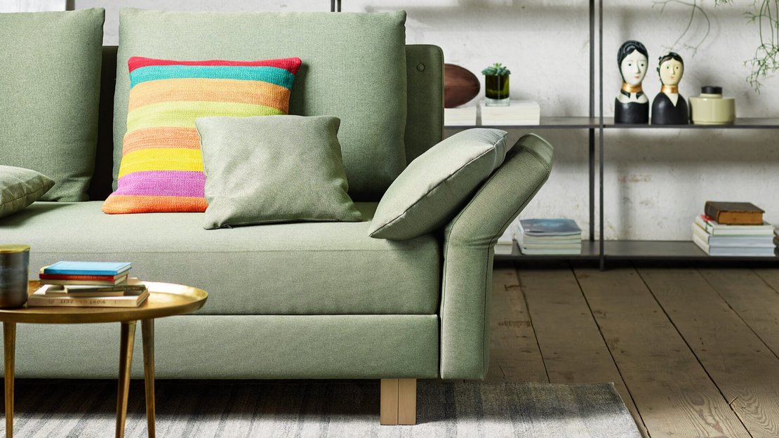 Grüne JOKA Forum Doppelliege mit einem abklappbaren Armteil im Detail, dekoriert mit einem farbenfrohen gestreiften Kissen und einem kleinen grünen Kissen auf der Sitzfläche.