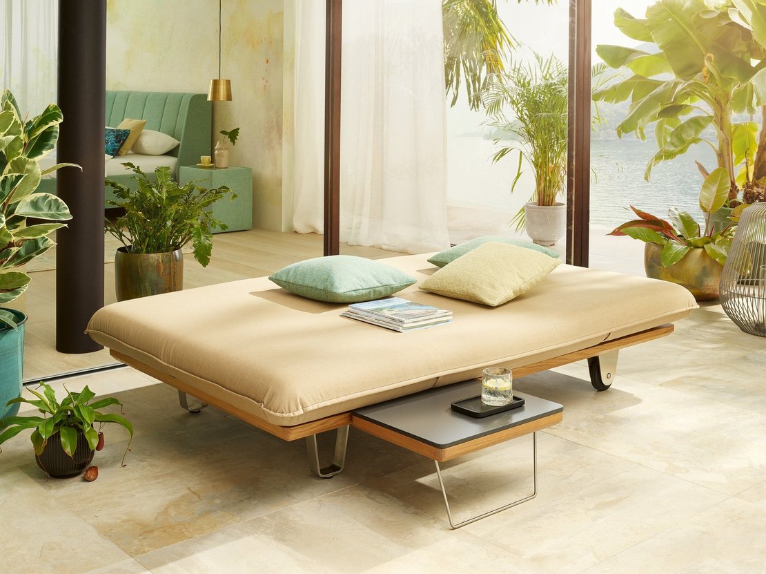 Das Bild zeigt das JOKA Butterfly Sunbed in flacher Position mit einem integrierten kleinen Tisch.