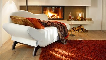 Geschwungenes Recamiere-Sofa in Weiß mit dunklen Holzbeinen und rustikaler Decke vor Kamin