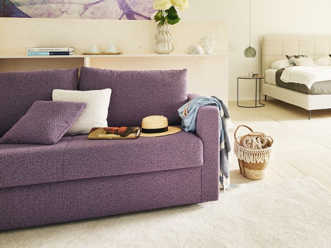 JOKA Mattina Bett in Beige mit lila Schlafsofa Onda und Sesseln in einer lichtdurchfluteten Suite