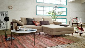 Loft-Wohnzimmer mit der beigen Eckcouch, bei der beide Segmente zu einer großzügigen Doppelliege vorgezogen sind.