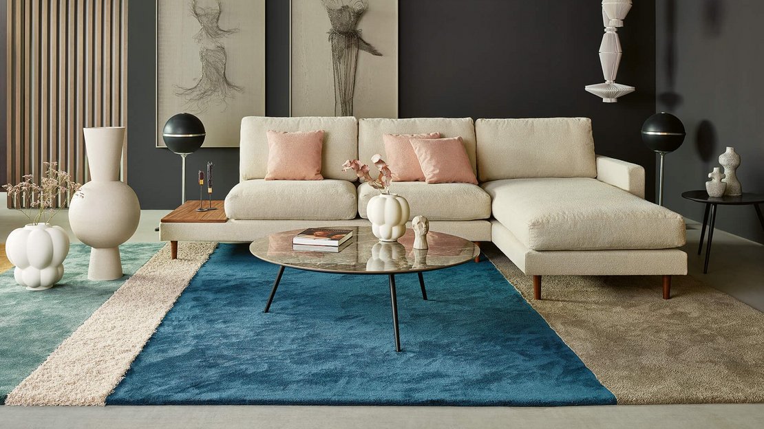 Querformatige Gesamtaufnahme derselben hellem Eckcouch-Konfiguration mit Holzablage, breiter Chaiselongue und Couchtisch.