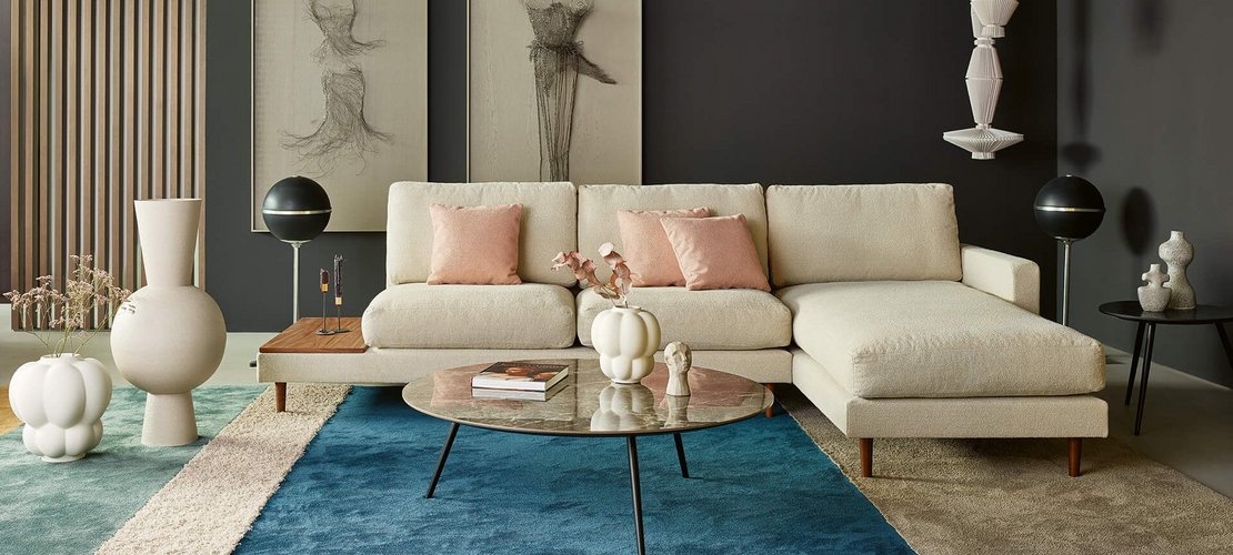 Querformatige Gesamtaufnahme derselben hellem Eckcouch-Konfiguration mit Holzablage, breiter Chaiselongue und Couchtisch.