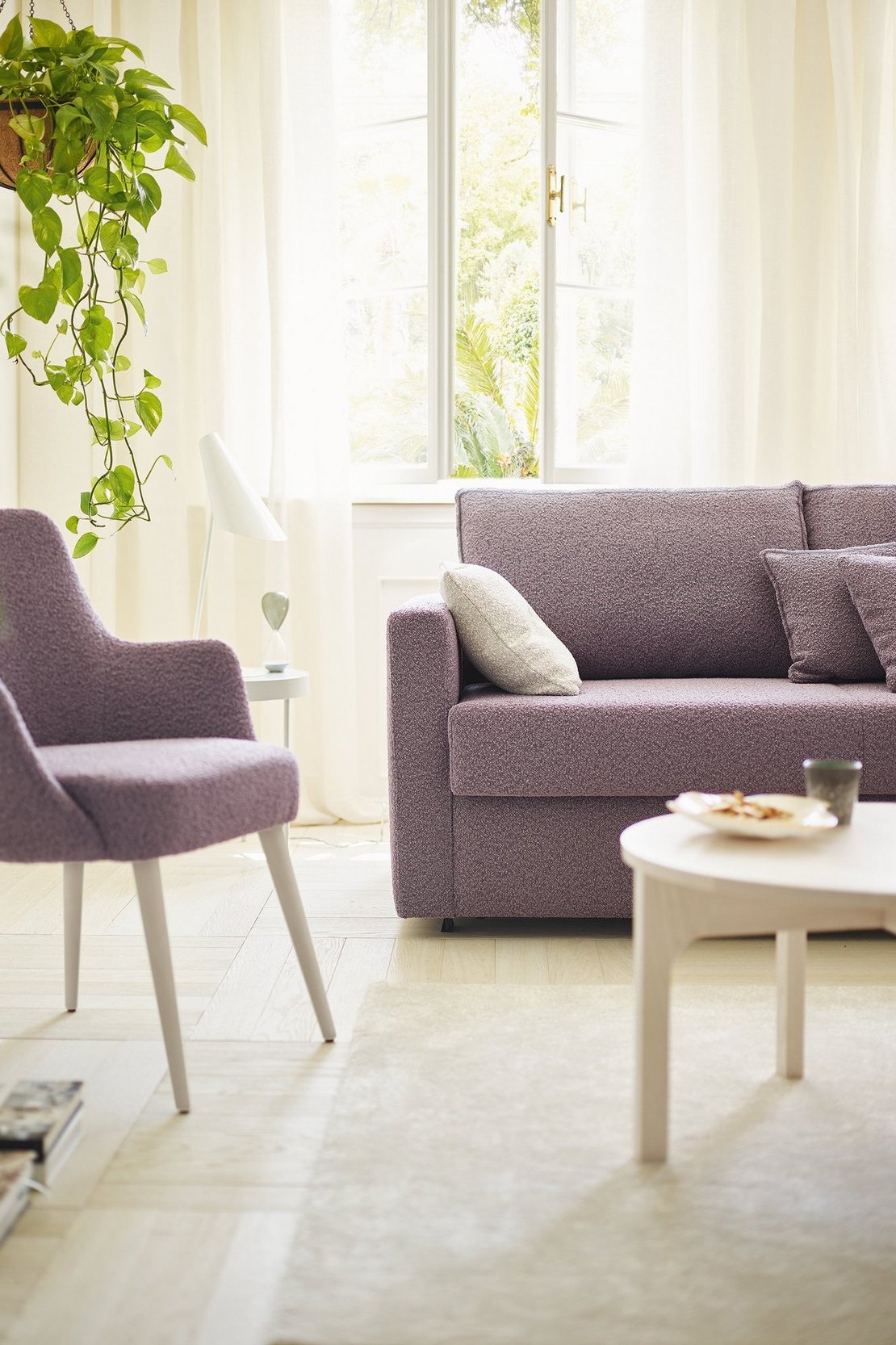 OKA Onda Doppelliege in Lila im Wohnzimmer mit passendem Sessel und Pflanzen.