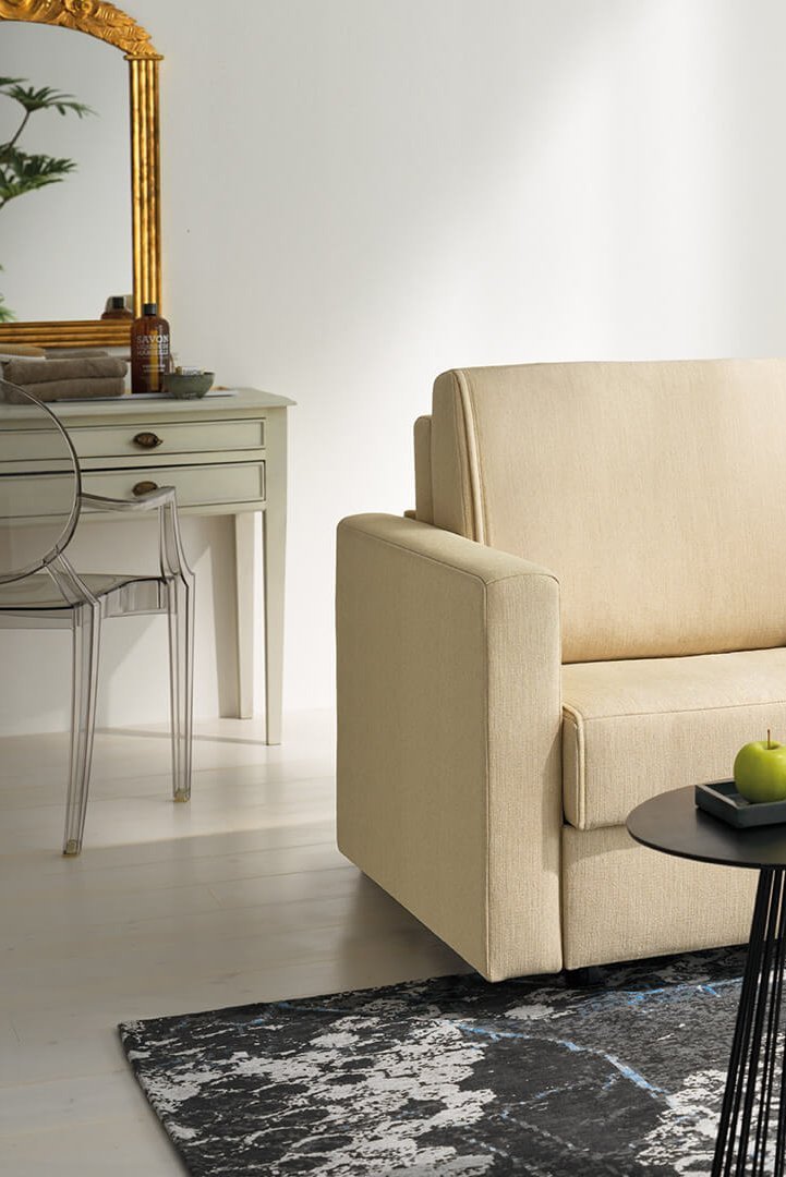 joka-magic-laengsschlaefer.jpg: Beige JOKA Magic Längsschläfer Couch dekoriert mit dunklen und hellen Zierkissen in einem hellen Wohnraum mit gemustertem Teppich und schwarzen Beistelltischen.
