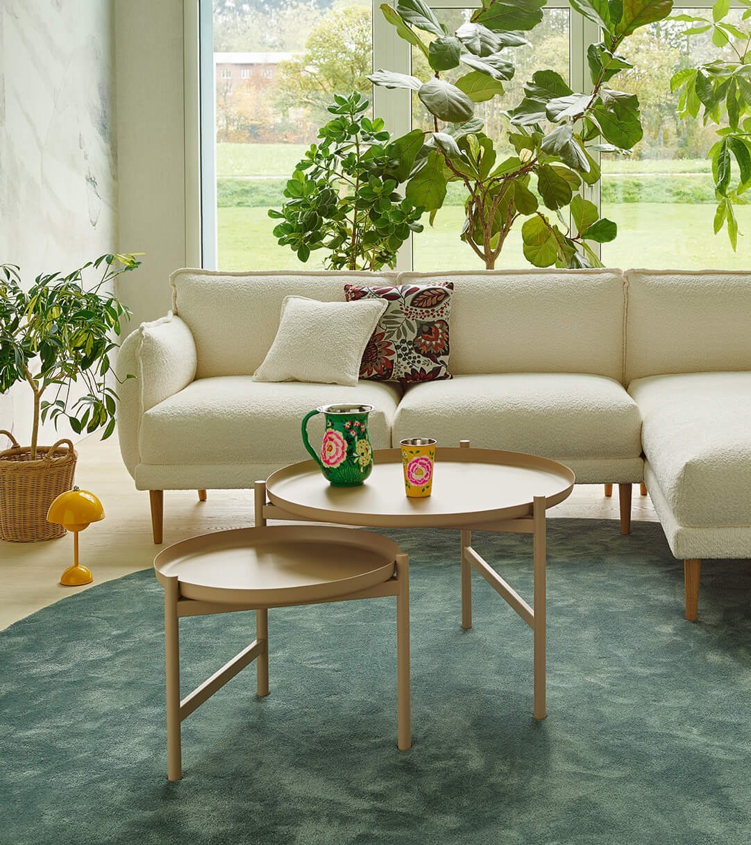 Weißes Bouclé-Sofa (2-Sitzer mit Chaiselongue) auf einem grünen runden Teppich in einem von Pflanzen umgebenen Raum.