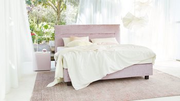 JOKA Capri Boxspringbett in Altrosa mit weißer Bettwäsche in einem lichtdurchfluteten Raum