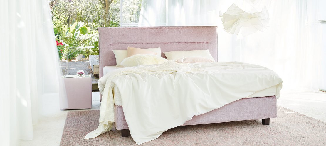 JOKA Capri Boxspringbett in Altrosa mit weißer Bettwäsche in einem lichtdurchfluteten Raum