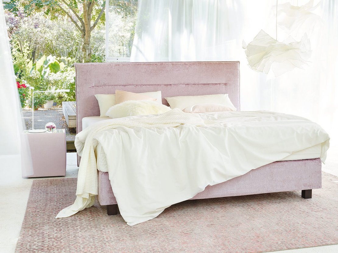 JOKA Capri Boxspringbett in Altrosa mit weißer Bettwäsche in einem lichtdurchfluteten Raum